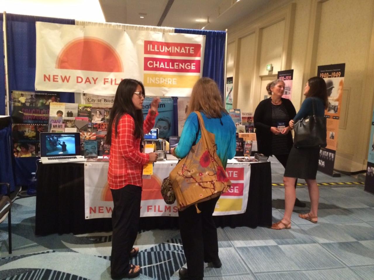 Two New Day Films filmmakers converse with conference attendees at the booth.