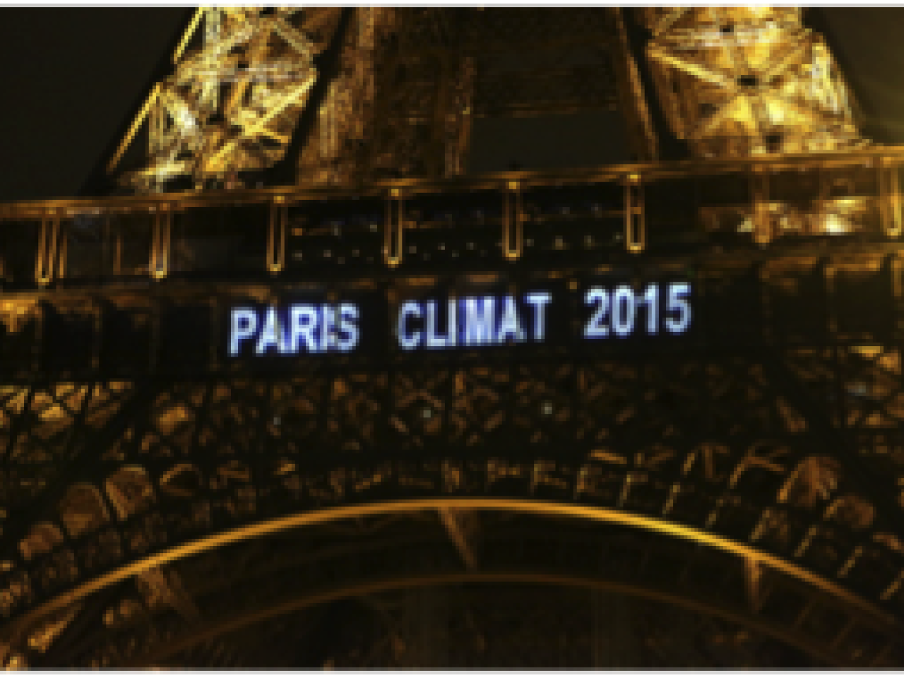 A close up image of the Eiffel tower at night with the words “Paris Climat 2015” projected in white letters on it.