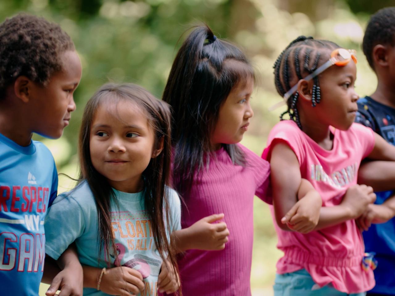 In this still from the film Upstream, Downriver, a group of children are outdoors linking arms.