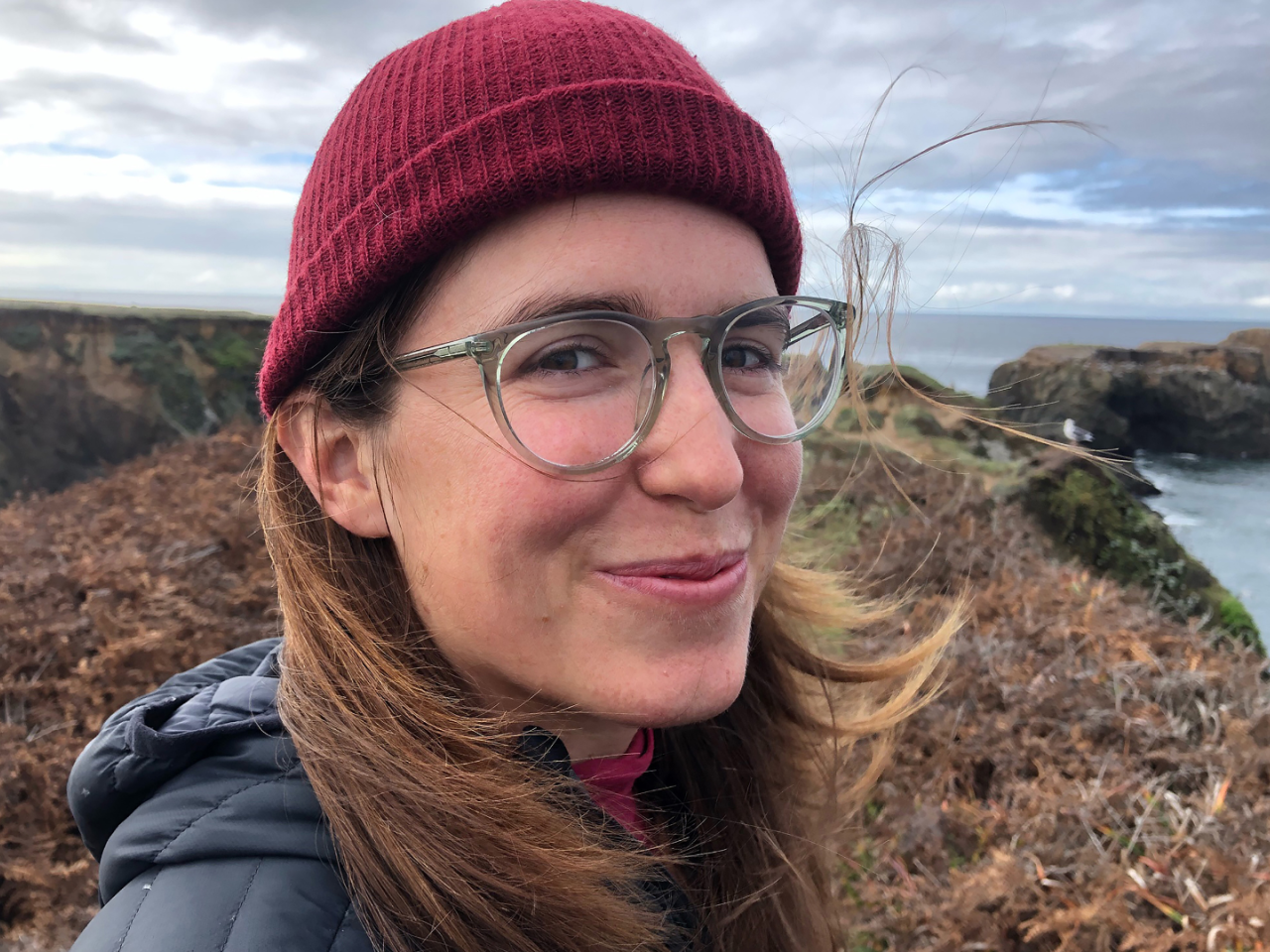 Headshot of Amy Reid outside. She has long hair, glasses, and a red beanie.