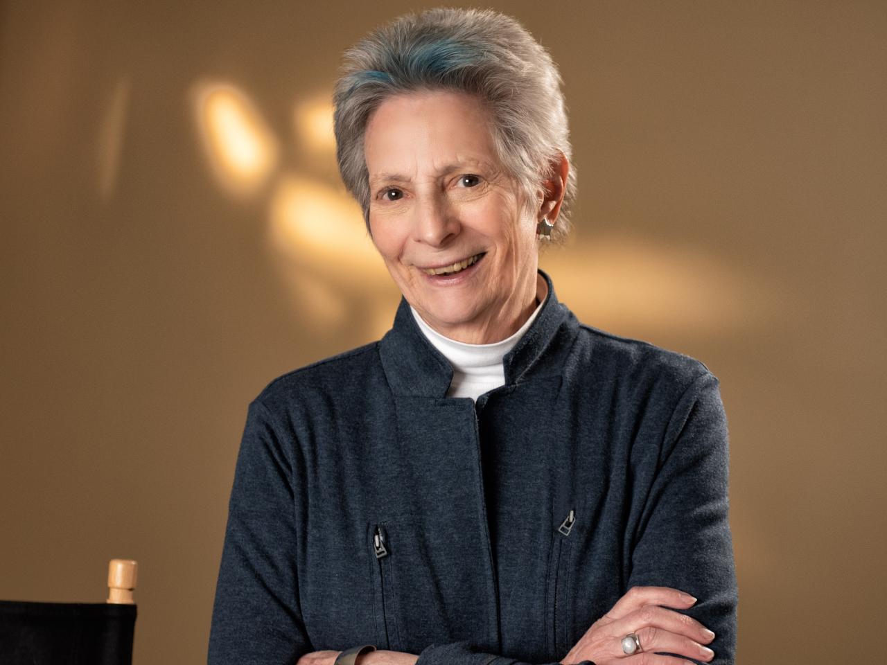 A woman with short, grey hair looks at the camera and smiles.