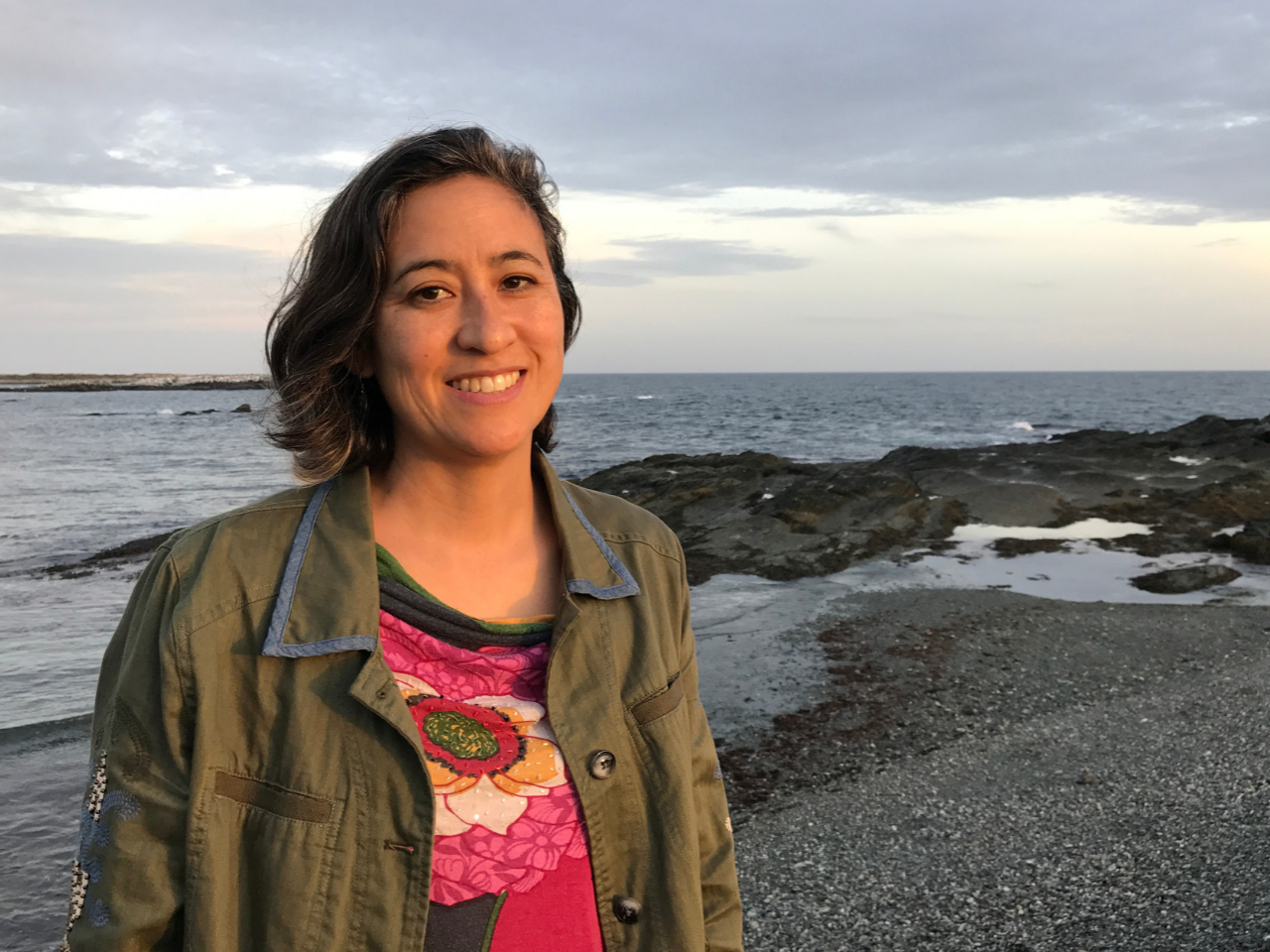 Filmmaker Julie Mallozzi is on the beach with the sun on her face. She is smiling. 