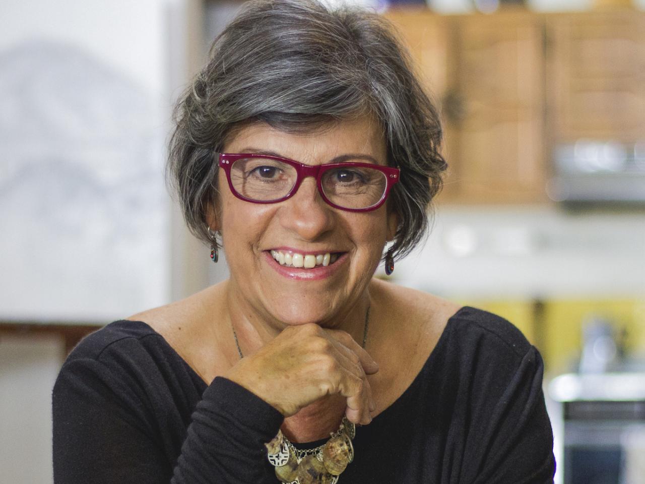 Photo of filmmaker Luisa de la Ville looking into the camera and smiling. They have short, graying hair and red glasses.