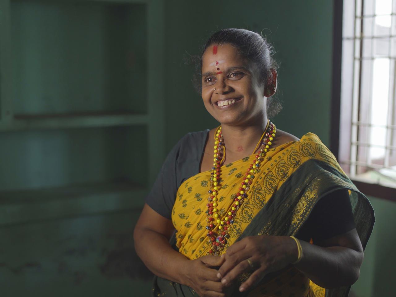 An Indian woman in a vibrant yellow and green sari, smiling radiantly.