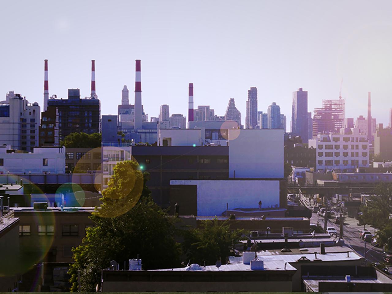 Wide angle shot of a city showing power plant chimneys and an elevated train line.