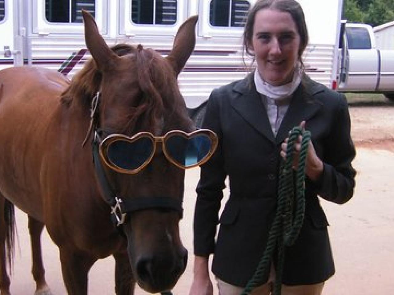 Woman standing next to a horse with huge sunglasses on.