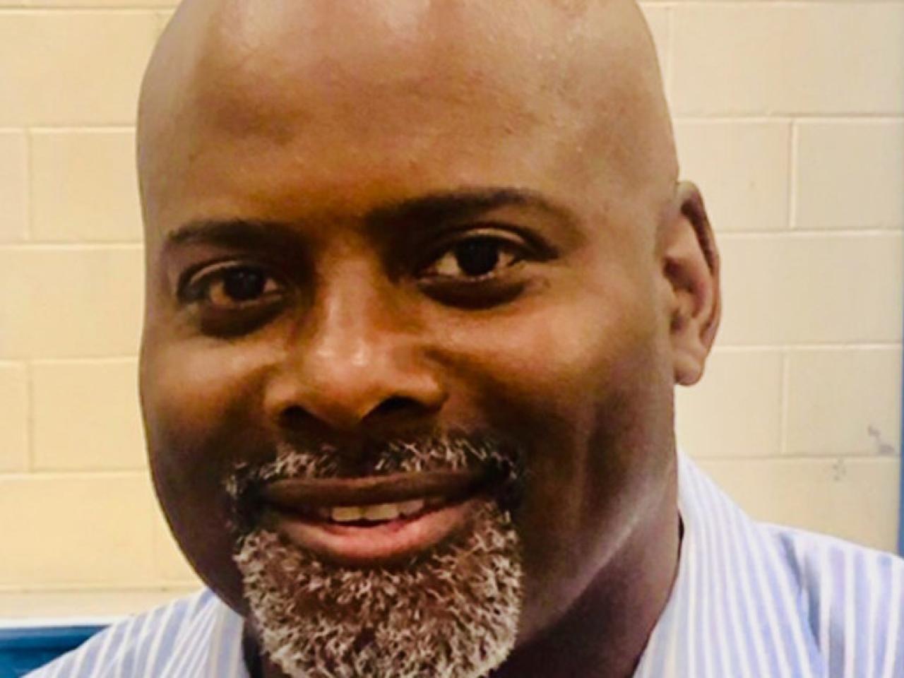 A headshot of New Day Filmmaker Mike Mascoll, a bald African-American man with a grey goatee. He looks directly at the camera and smiles.