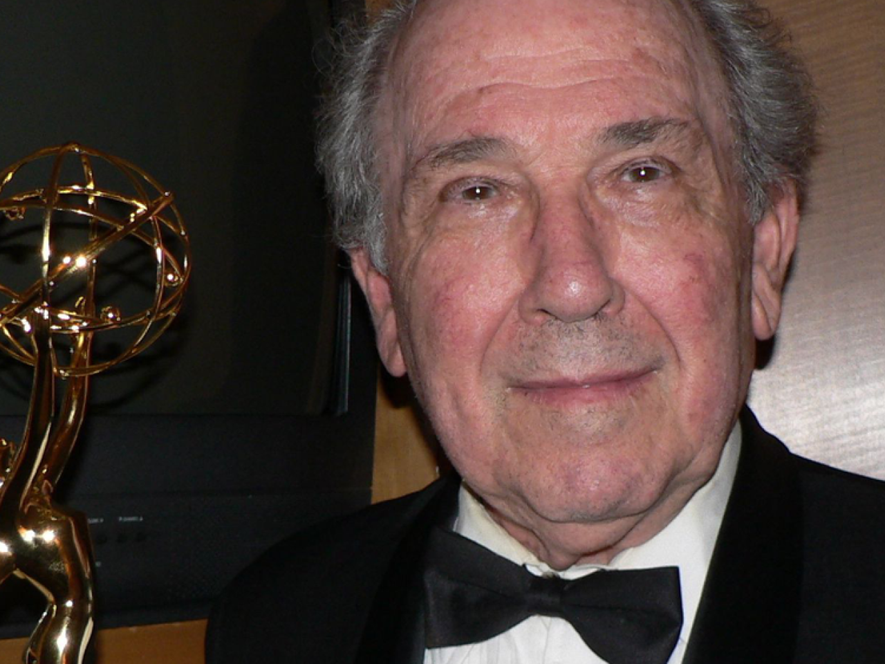 Filmmaker Robert Richter looks at the camera with a slight smile. He is dressed in a black tux. A gold Emmy statue is to his left.