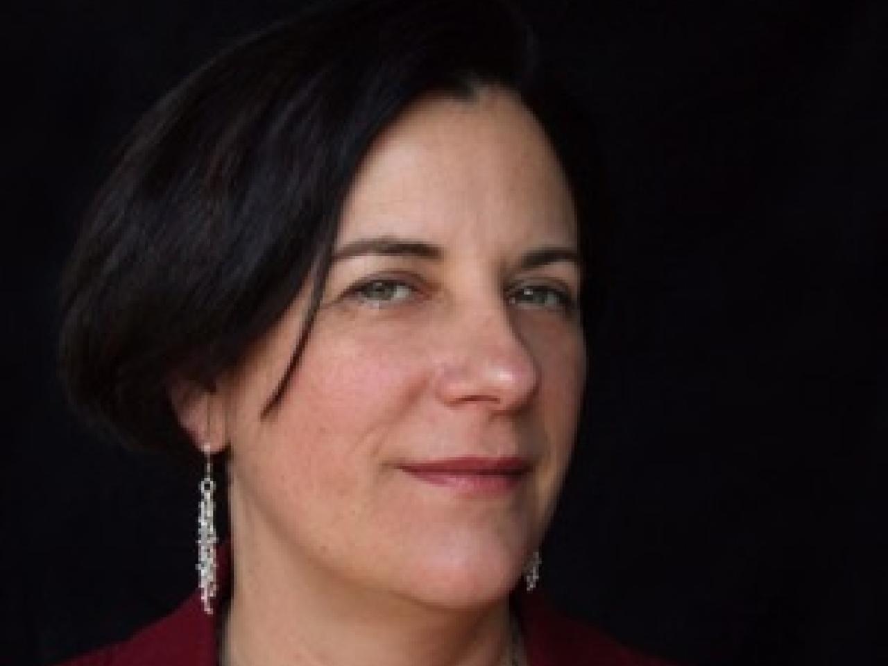 A headshot of the New Day filmmaker Dawn Logsdon. She looks at the camera with a knowing confident smile and she with long dangly earrings.