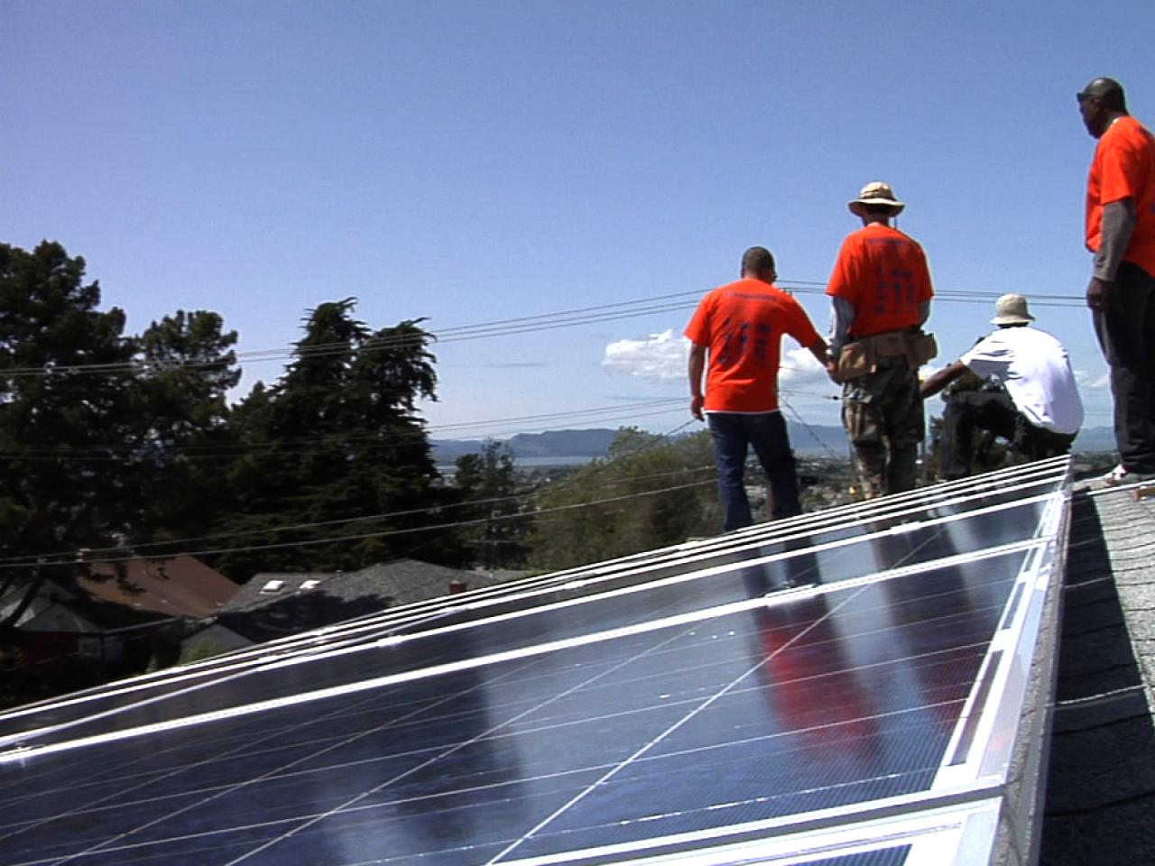 An image from the film Catching the Sun of workers in jeans and red t-shirts installing solar panels on a building's roof.